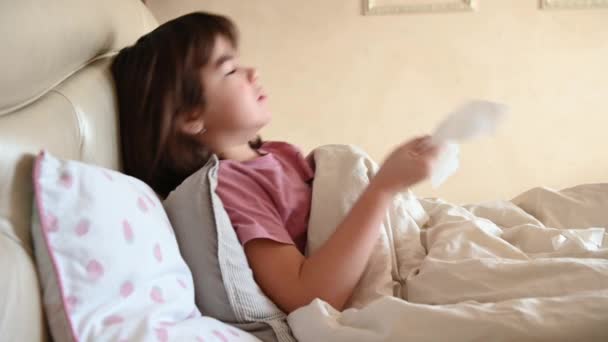 10-летняя девочка лежит больная в постели, кашляет, высморкается в салфетку — стоковое видео