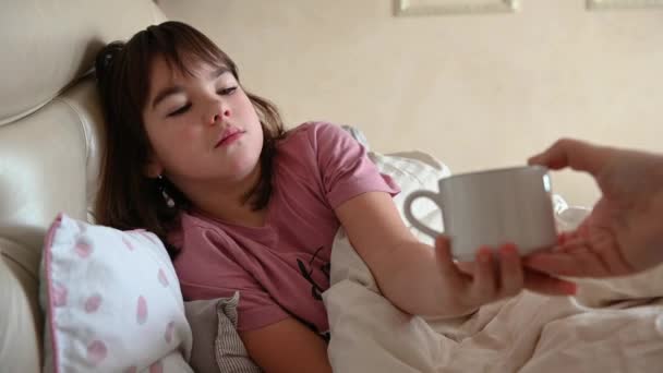 10-летняя девочка лежит в постели больная, кашляет, пьет чай — стоковое видео