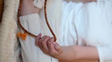 dikey video. Bir adam lotus pozisyonunda oturur. Tespihi parmaklayan ellerin yakın çekimi. izoterik tema