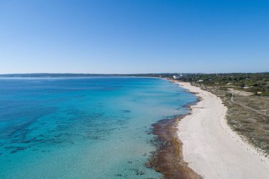 Güneşli bir günde insansız hava aracından görülen turkuaz suları ve beyaz kumları olan bir sahil.