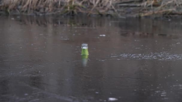 Бутылка стекла застряла в льду, загрязнение воды и мусор в природе зимой — стоковое видео