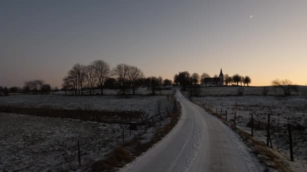 Landelijke weg leidt naar de kerk in de winter met zonsondergang en halve maan in de lucht — Stockvideo