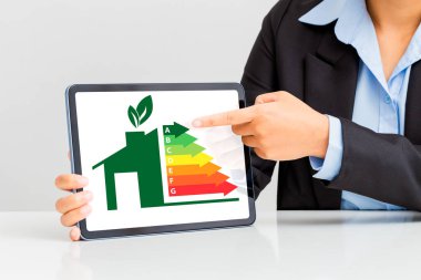 Kadın eli tablet ekranlardaki ev verimliliği oranını gösteriyor. Enerji verimliliği ve yeşil enerji kavramı, çevre kavramı.