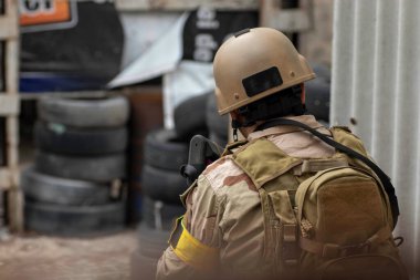 Hava yumuşaklığı oyunu, üniformalı ve kasklı bir oyuncu, hava yumuşaklığında bir silahla, özel bir oyun alanında, eski tekerlerden korunaklı sığınaklar.