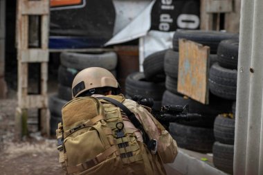Hava yumuşaklığı oyunu, üniformalı ve kasklı bir oyuncu, hava yumuşaklığında bir silahla, özel bir oyun alanında, eski tekerlerden korunaklı sığınaklar.