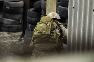 Hava yumuşaklığı oyunu, üniformalı ve kasklı bir oyuncu, hava yumuşaklığında bir silahla, özel bir oyun alanında, eski tekerlerden korunaklı sığınaklar.