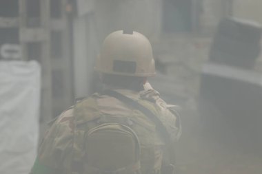 Hava yumuşaklığı oyunu, üniformalı ve kasklı bir oyuncu, hava yumuşaklığında bir silahla, özel bir oyun alanında, eski tekerlerden korunaklı sığınaklar.