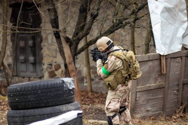 Hava yumuşaklığı oyunu, üniformalı ve kasklı bir oyuncu, hava yumuşaklığında bir silahla, özel bir oyun alanında, eski tekerlerden korunaklı sığınaklar.