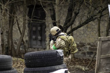 Hava yumuşaklığı oyunu, üniformalı ve kasklı bir oyuncu, hava yumuşaklığında bir silahla, özel bir oyun alanında, eski tekerlerden korunaklı sığınaklar.