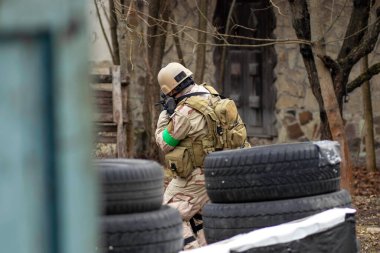 Hava yumuşaklığı oyunu, üniformalı ve kasklı bir oyuncu, hava yumuşaklığında bir silahla, özel bir oyun alanında, eski tekerlerden korunaklı sığınaklar.
