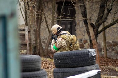 Hava yumuşaklığı oyunu, üniformalı ve kasklı bir oyuncu, hava yumuşaklığında bir silahla, özel bir oyun alanında, eski tekerlerden korunaklı sığınaklar.