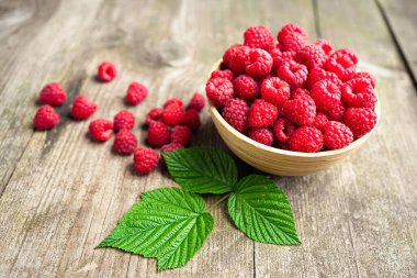 Köhne ahşap masadaki bir kasede yaprakları olan taze kırmızı ahududular. Sağlıklı organik yiyecekler, yaz vitaminleri, BIO virüsleri, doğal arka plan. Reklam metniniz için alanı kopyalayın.