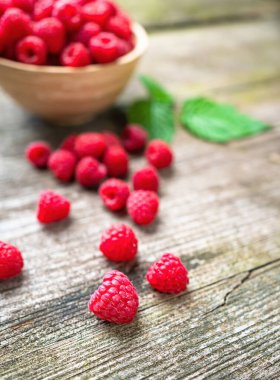 Köhne ahşap masadaki bir kasede yaprakları olan taze kırmızı ahududular. Sağlıklı organik yiyecekler, yaz vitaminleri, BIO virüsleri, doğal arka plan. Reklam metniniz için alanı kopyalayın.