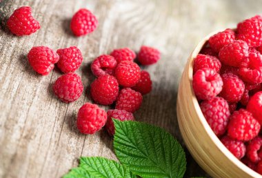 Köhne ahşap masadaki bir kasede yaprakları olan taze kırmızı ahududular. Sağlıklı organik yiyecekler, yaz vitaminleri, BIO virüsleri, doğal arka plan. Reklam metniniz için alanı kopyalayın.