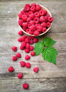 Köhne ahşap masadaki bir kasede yaprakları olan taze kırmızı ahududular. Sağlıklı organik yiyecekler, yaz vitaminleri, BIO virüsleri, doğal arka plan. Reklam metniniz için alanı kopyalayın.