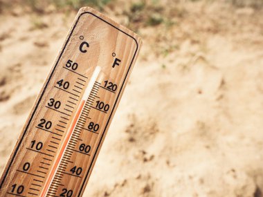 Wooden thermometer showing high temperatures over 36 degrees Celsius on sunny day on background of dry sandy ground. Concept of heat wave, warm weather, global warming, climate.