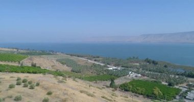 Golan Tepeleri ve Tiberias 'ın yukarısında gün batımında Celile Denizi ya da İsrail' in kuzeyindeki Ürdün Vadisi 'nde Kinneret ile hava görüntüleri. Turuncu yeşil manzaralı ve berrak dağlı açık arazilerin üzerinde insansız hava aracı