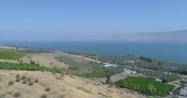 Golan Tepeleri ve Tiberias 'ın yukarısında gün batımında Celile Denizi ya da İsrail' in kuzeyindeki Ürdün Vadisi 'nde Kinneret ile hava görüntüleri. Turuncu yeşil manzaralı ve berrak dağlı açık arazilerin üzerinde insansız hava aracı — Stok video