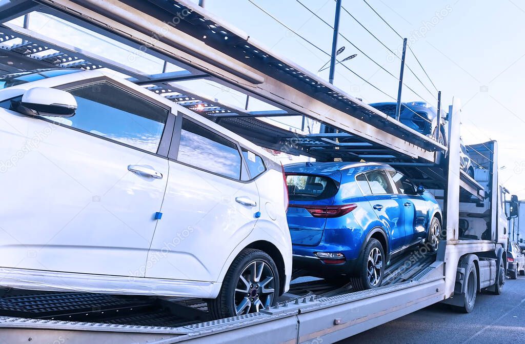 An auto transporter carries white and blue cars along the road. Important and responsible work.