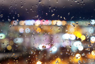 Gece penceresindeki yağmur damlaları şehir ışıklarının arka planına karşı.            