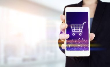 Internet Cart Web Mağazası Çevrimiçi E-Ticaret konsepti satın al. El ele tutuşan beyaz akıllı telefon. Arka planda ışık bulanık, dijital hologram arabası işareti var. Çevrimiçi alışveriş teknolojisi İnternet kavramı
