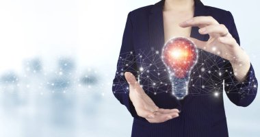 Yaratıcı fikir. Fikir ve yenilik kavramı. İki el, arka planda bulanık ışık bulunan sanal holografik ampul ikonunu tutuyor. Ampulle ağ parlak fikri.