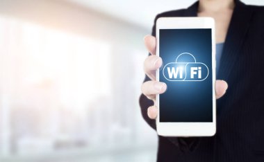 Kablosuz internet kavramı. El ele tutuşan beyaz akıllı telefon, arka planda bulanık ışık üzerinde dijital hologram Wi-Fi işareti var. Ücretsiz WiFi ağ sinyal teknolojisi internet kavramı