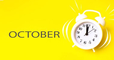 Ekim. Bir ay, takvim ayı. Sarı arka planda takvim günü olan beyaz çalar saat. Asgari zaman kavramı, son teslim tarihi, çalışma zamanı, sabah. Sonbahar, yılın ayı konsepti.