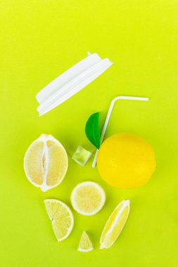 Fresh organic ice tea in abctract paper cup glass with yellow lemon lime fruit slice and green leaves, ice cube, straw on light green background. Summer refreshing drink