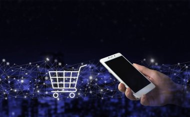 Çevrimiçi alışveriş, akıllı telefondan online mağaza uygulaması. Şehrin karanlık arka planında dijital hologram arabası işareti olan el kameralı beyaz bir akıllı telefon. E-ticarette yenilik kavramı