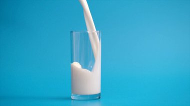 mavi zemin üzerine bir bardak içine dökülen süt