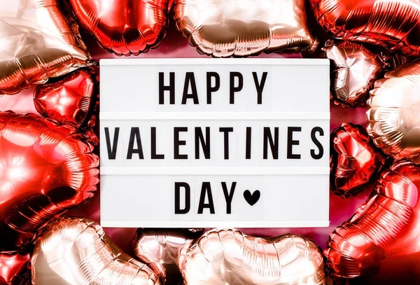 Stylish text frame lightbox with the inscription happy Valentine's day. Red and beige hearts all around. Foil balloons top view of Valentine's Day. Copyspace.