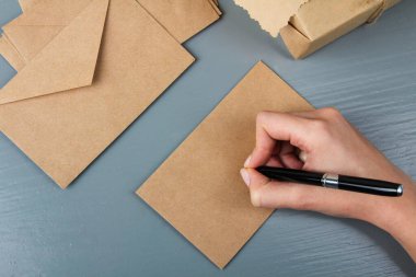 Gri ahşap arka plandaki harfler için zarfı imzalayacak kadın.