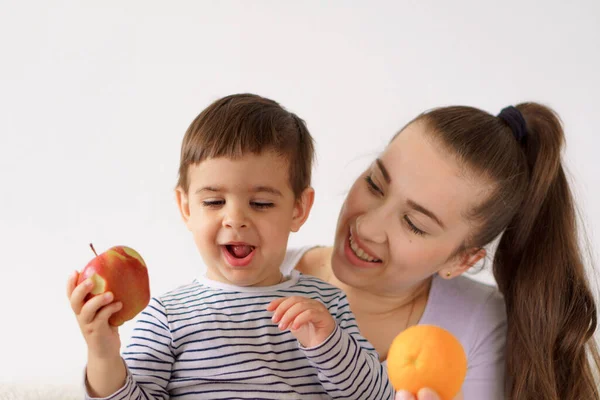 Vrolijke vrolijke grappige moeder met peuter zoon jongen jongen eten vers fruit groenten thuis. familie eet lunch sinaasappels, citrusappels bananen. Gezond eten, vitaminen, dieet, vegetarisme menu concepten — Stockfoto