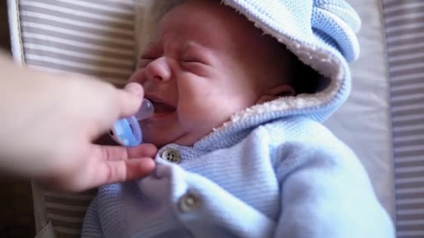 Lihat bayi di kamera close up shot. bayi, masa kecil, cinta orang tua, konsep emosi - wajah lucu tersenyum dari bayi bermata gemulai yang baru lahir dengan jaket biru lembut terjaga. tangan wanita memberikan dot untuk bayi. — Stok Video