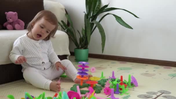 Szczęśliwy śmieszne dziecko kręcone dziewczynka z edukacyjnych zabawek blokuje kwiaty. Dzieci bawią się w przedszkolu lub żłobku. Bałagan w pokoju dziecięcym. Maluch buduje wieżę w przedszkolu. Dziecko bawi się kolorowymi zabawkami — Wideo stockowe