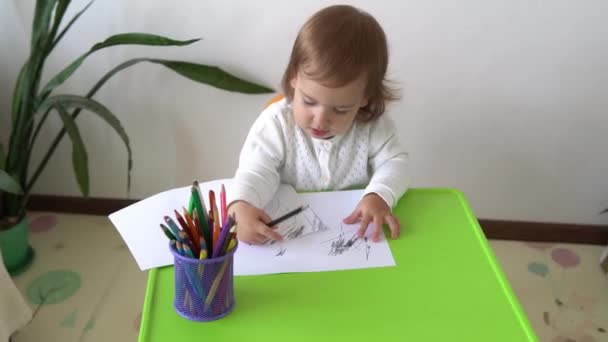 Onderwijs Kaukasisch klein kind dochter gelukkig grappig kind krullend baby meisje met tekeningen aan tafel. geconcentreerde creatieve peuter schrijft met gekleurde potloden op papier kids kamer. hobbystudie thuis — Stockvideo