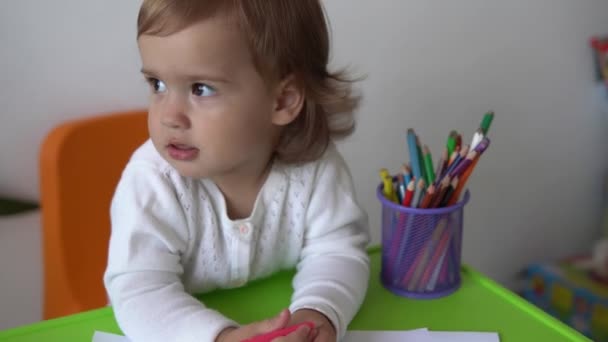 Close-up Kaukasische kleine kind dochter gelukkig grappig kind krullend baby meisje met tekeningen aan tafel. geconcentreerde creatieve peuter schrijft met gekleurde potloden op papier kids kamer. hobbystudie thuis — Stockvideo