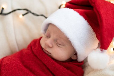 Yeni doğanların ilk portresi. Beyaz çelenk arka planında kırmızı beze sarılı, tatlı, uyuyan, Noel Baba şapkalı bebek. Mutlu Noeller, Mutlu yıllar, Bebek, Çocukluk, Kış