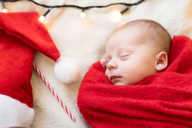 Yeni doğan bebeğin ilk portresi beyaz çelenk arka planında kırmızı bebek bezi halısına sarılı Noel Baba Şapkalı Güzel Uyuyan Bebek. Mutlu Noeller, Mutlu yıllar, Bebek, Çocukluk, Kış Konsepti