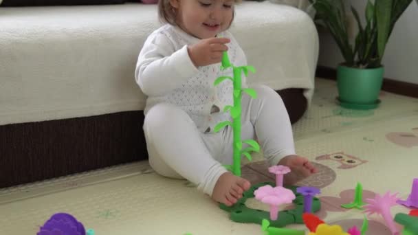 Šťastný legrační dítě kudrnaté holčička se vzdělávací hračka bloky květiny. Děti si hrají ve školce nebo ve školce. Zahrávat si v dětském pokoji. Batole postavilo věž ve školce. Dítě si hraje s barevnými hračkami — Stock video