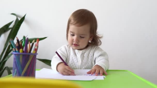 Közelkép kaukázusi kisgyerek lánya boldog vicces gyerek göndör kislány rajzol képet az asztalnál. koncentrált kreatív kisgyerek ír színes ceruzával papírgyerekszoba. hobbitanulás otthon — Stock videók