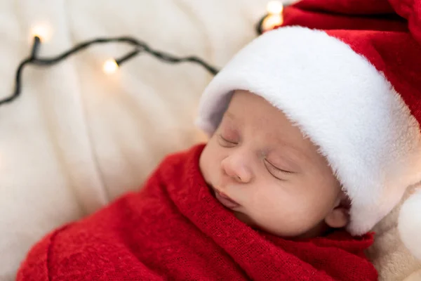 Yeni doğanların ilk portresi. Beyaz çelenk arka planında kırmızı beze sarılı, tatlı, uyuyan, Noel Baba şapkalı bebek. Mutlu Noeller, Mutlu yıllar, Bebek, Çocukluk, Kış Stok Resim