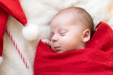 Yeni doğan bebeğin ilk portresi beyaz çelenk arka planında kırmızı bebek bezi halısına sarılı Noel Baba Şapkalı Güzel Uyuyan Bebek. Mutlu Noeller, Mutlu yıllar, Bebek, Çocukluk, Kış Konsepti
