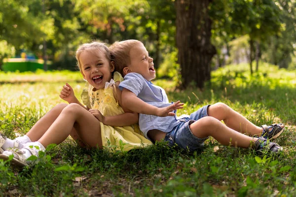 Mutlu gülümseyen iki çocuk anaokulu ikizi iki kardeş kardeş kardeş kardeş kardeş kız kardeş güneşli yaz havasında parkta çimlerin üzerinde birlikte oturuyorlar. çocukluk, arkadaşlık, aile kavramı Telifsiz Stok Fotoğraflar