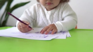 Kafkasyalı küçük çocuk kız mutlu, kıvırcık kız bebek masada resim çiziyor. Yaratıcı çocuk kağıt çocuk odasında renkli kalemlerle yazı yazıyor. evde hobi eğitimi.