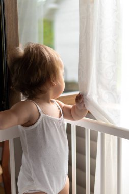 Küçük, şirin, mutlu bir bebek bebek bebek, beyaz pijamayla beyaz bir beşikte tatlı tatlı uyuyor ve küçük yastıklı çocuk sıcak yaz gününde sıcak bir pencereden dışarı bakıyor. Çocukluk konsepti. Boşluğu kopyala