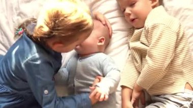 Çocukluk, çocukluk, aile, uyku, dinlenme konsepti - üç mutlu çocuğa yakın çekim, yeni doğan bebek ve 3-4 yaşındaki kız kardeşler bej beyaz yatakta birlikte oynuyorlar. Kız kardeşler evde oynuyorlar..