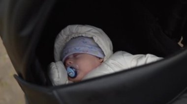 Çocukluk, çocukluk, kış. Küçük bebek, siyah bebek arabasında sıcak bir ceketle uyuyor. Annem soğuk sonbahar havasında parkta bebek arabasında uyuyan bebekle yürür.