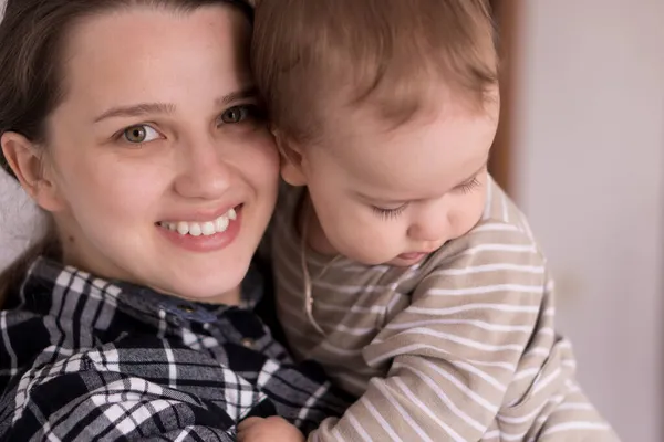 Retrato rosto adorável de pouco alegre criança bebê menina feliz com encantador sorriso olhar para a mãe forte abraços amando mamãe juntos. Mãe abraços jogar amor cuidado beijo sorrindo filha em casa — Fotografia de Stock